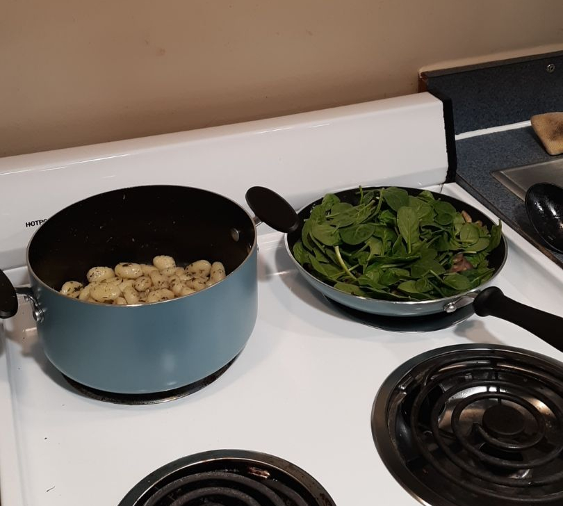 Image of a stovetop with a pot of gnocchi on one burner and a pan of spinach on another